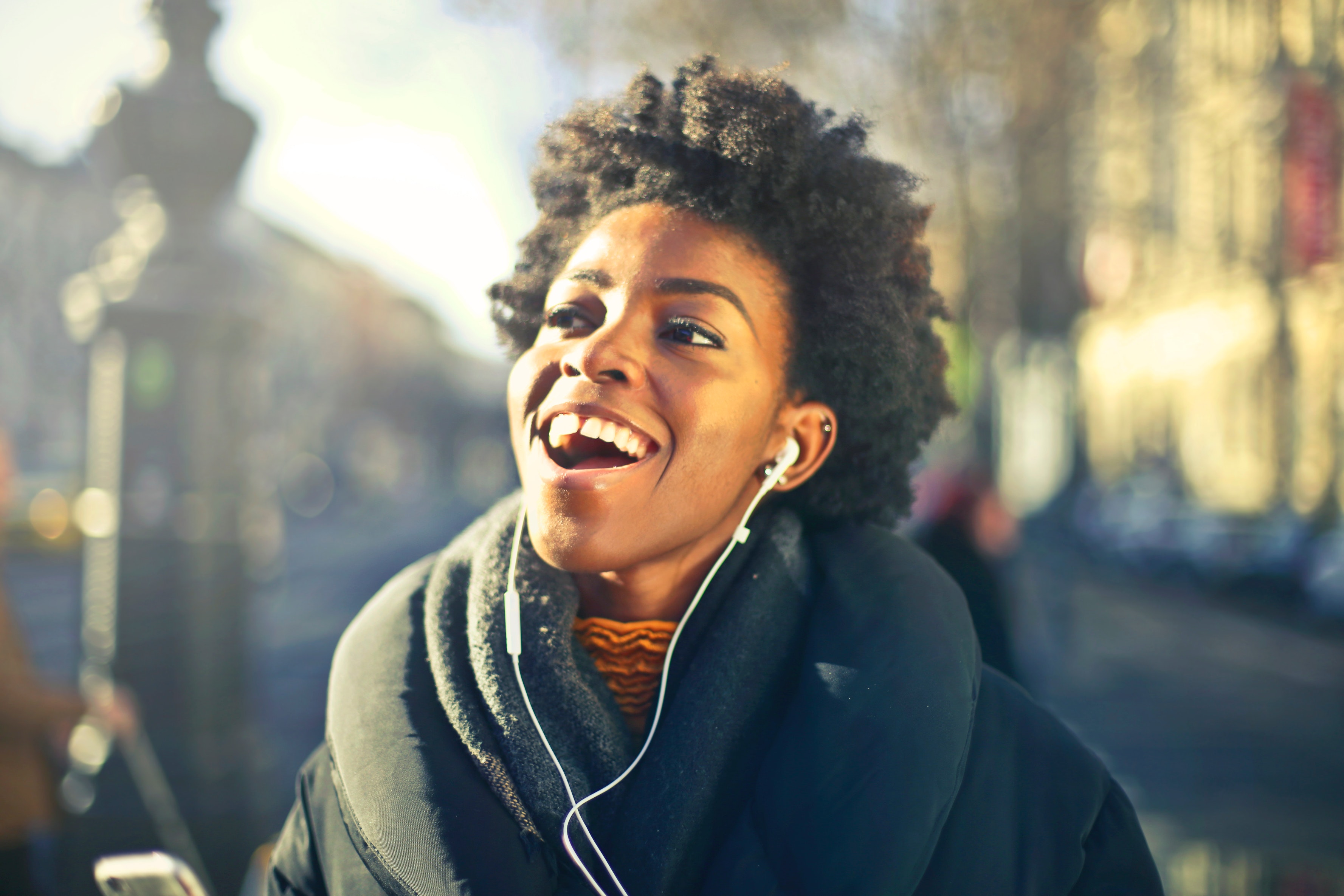 Picture of a black woman with earbuds looking up and smiling with her mouth open.