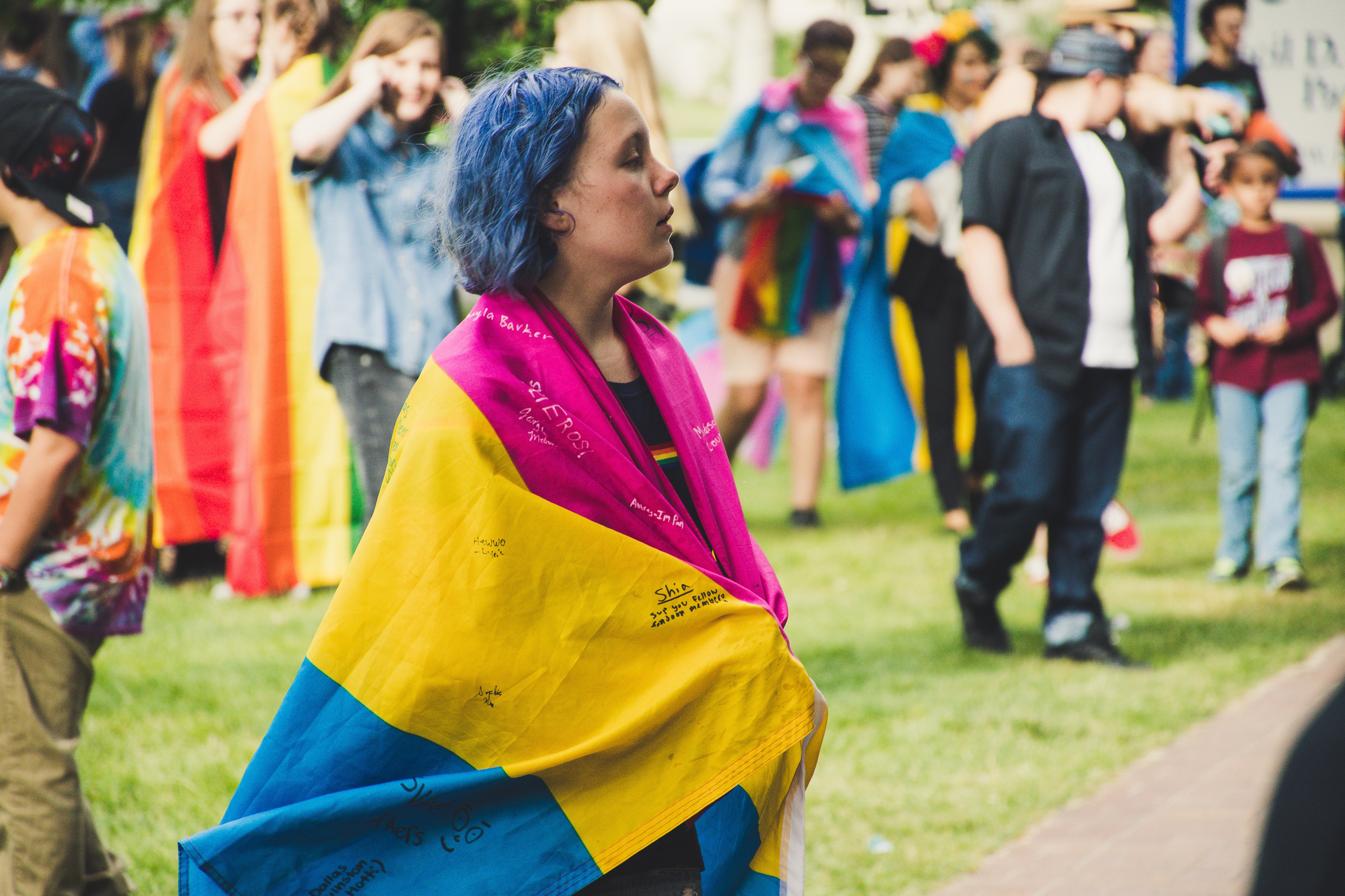 Woman wrapped in a large pansexual flag (bright pink, yellow, blue).